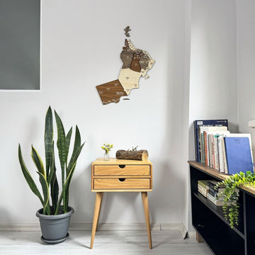 Carte d'Oman en bois au-dessus d'une table de chevet en bois et d'une plante en pot dans un coin