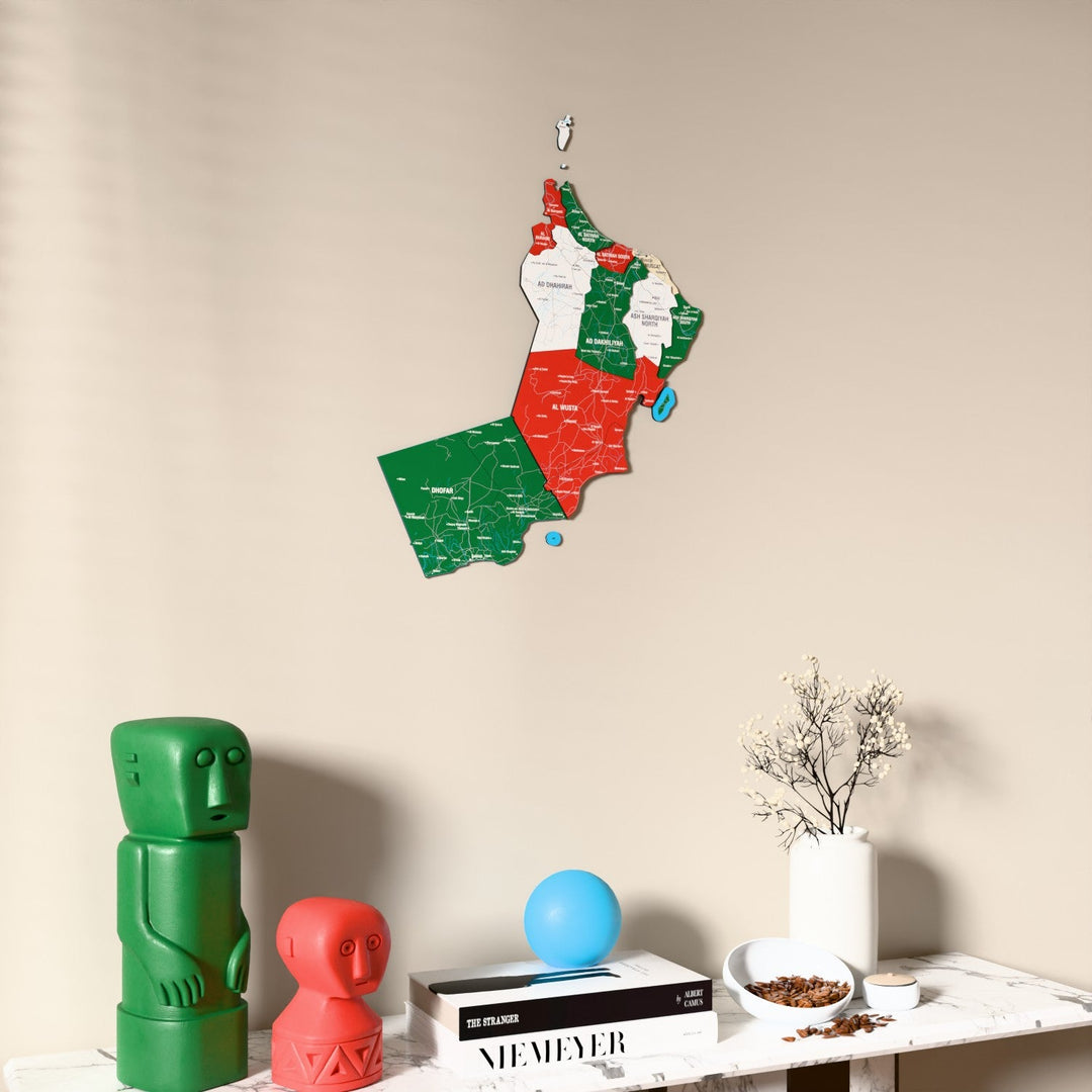 Flag colored Oman wooden wall map on a beige wall above a console with figurines
