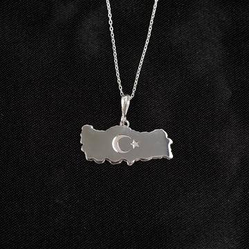 Silver Turkiye map necklace hanging straight against black fabric
