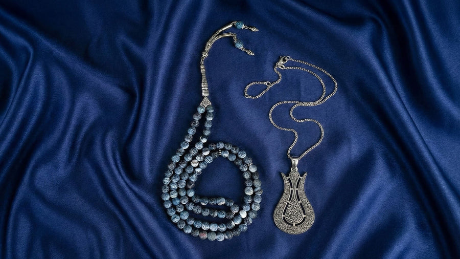 Gray prayer beads and a tulip-shaped Islamic pendant necklace on navy blue satin