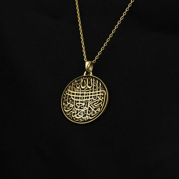 منظر مائل للدلاية الذهبية بدعاء الحماية من العين معلقة على سلسلة ذهبية أمام قماش أسود
