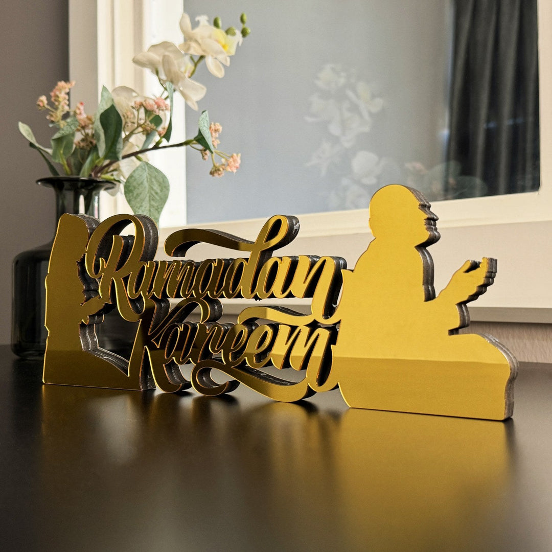 Close view of gold Ramadan Kareem decor with a praying figure in silhouette beside a flower vase