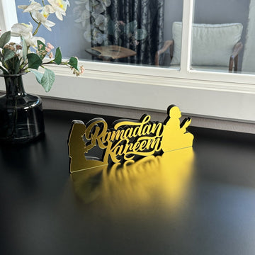 Gold Ramadan Kareem tabletop decor with praying figures seen from a distance beside a window