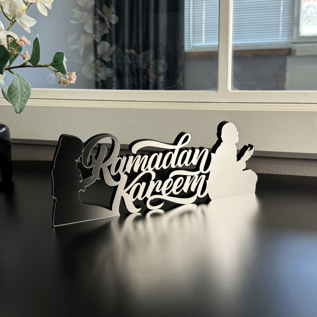 Silver Ramadan Kareem tabletop decor with a praying figure in silhouette on a dark table, side view