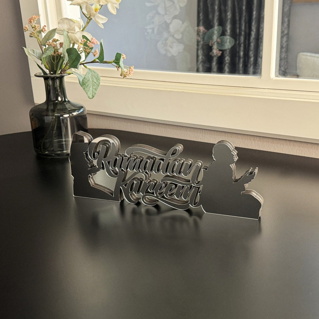 Silver Ramadan Kareem prayers detail tabletop decor on a black table, wide view with a vase of flowers