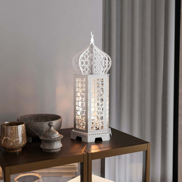 White Ramadan lantern metal decor lit from inside on a dark side table