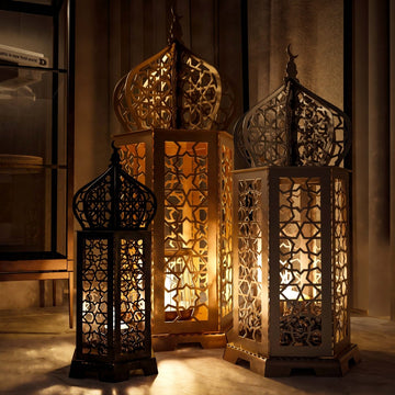 Three Ramadan lanterns in black, gold and white glowing together near dark curtains