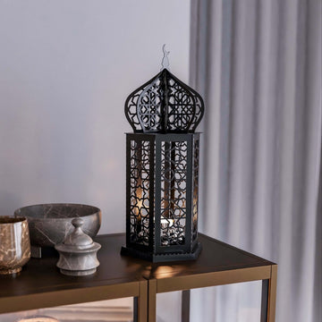 Black Ramadan lantern metal decor lit from inside on a dark side table