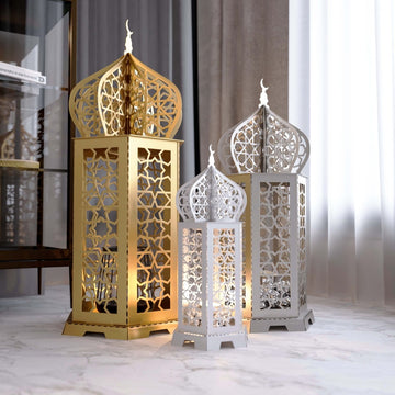 Ramadan lantern metal wall art set of three in gold and white on a marble floor, glowing from inside