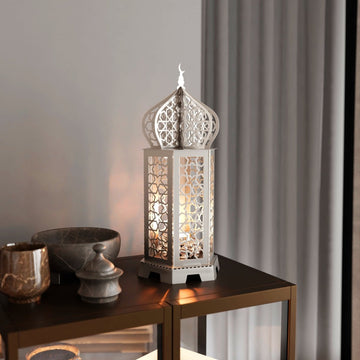Silver Ramadan lantern metal decor lit from inside on a dark side table beside stone bowls