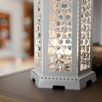 White Ramadan lantern shaft with star pattern cutouts and a lit candle, close view