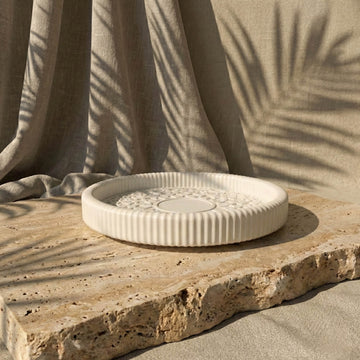 Decorative white ceramic plate on a stone surface with a beige curtain in the background