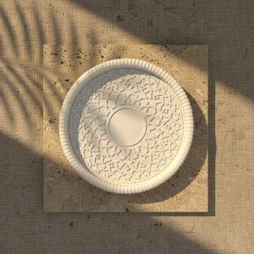 Decorative white ceramic bowl with intricate patterns on a textured beige surface