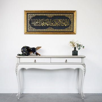 Framed Second Kalima wall art above a white console table with a Quran stand and flowers