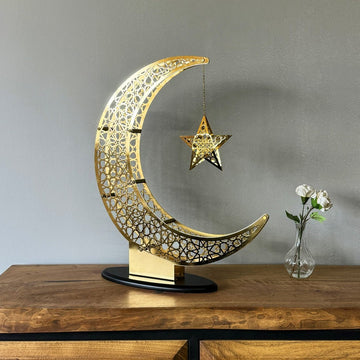Small Shiny Gold crescent and star decor on a wooden sideboard beside a glass bud vase