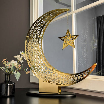 Shiny Gold metal crescent moon and star Islamic home decor on a black base beside a window