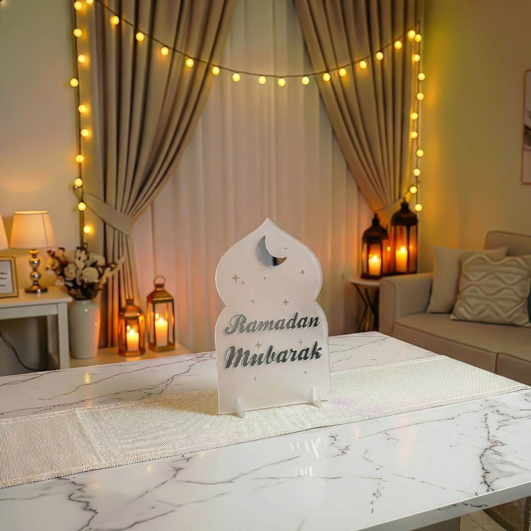 Ramadan-Mubarak-Aufsteller in Schrift-Design, Silber auf Frostweiß, auf einem Tisch, aus der Ferne gesehen