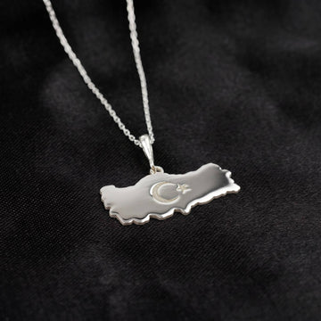 Silver Turkiye map pendant hanging from its chain, side view against black