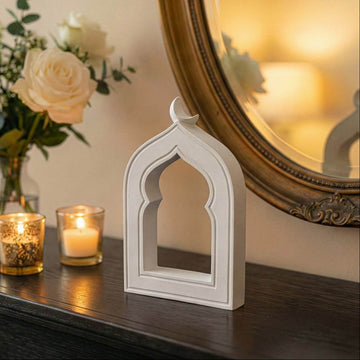 Stone mihrab arch with crescent moon on a dark console beside candles and a gold-framed mirror