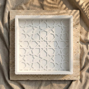 Draufsicht auf das quadratische weiße Steinrelief-Tablett mit maurischem geometrischem Muster auf einer Travertinplatte