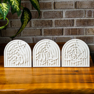 Three white stone dhikr arch plaques side by side on a wooden table, closer view
