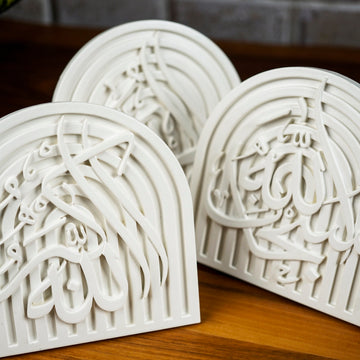 Close-up of three overlapping white stone dhikr arch plaques showing the relief calligraphy