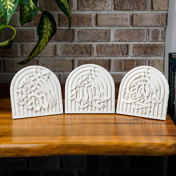 Three white stone dhikr arch plaques in a row on a wooden table, front view