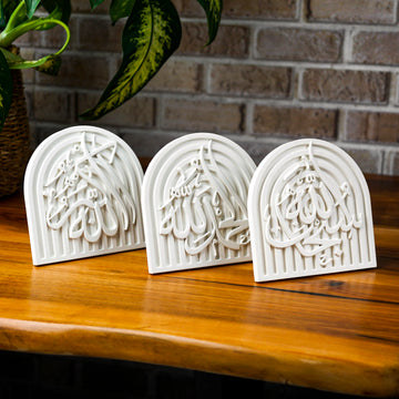 Set of 3 white stone dhikr arch plaques on a wooden table in front of a brick wall