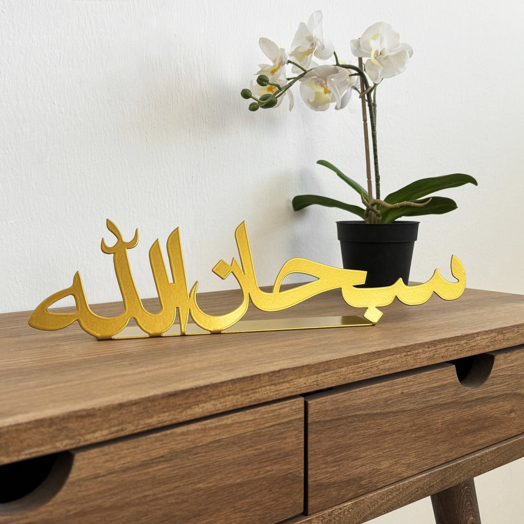 ديكور طاولة معدني ذهبي «سبحان الله» على مكتب خشبي، منظر أمامي مع زهرة أوركيد في أصيص