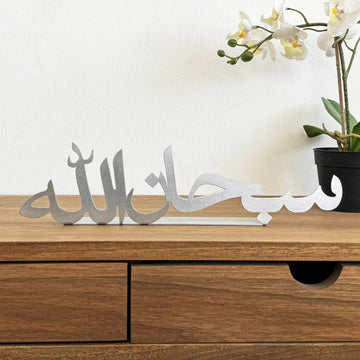 ديكور طاولة معدني فضي «سبحان الله» على مكتب خشبي، منظر أمامي مع زهرة أوركيد في أصيص