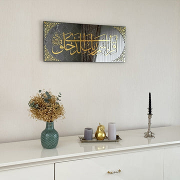 Surah Al-Alaq glass wall art with gold calligraphy hung above a white console in a bright room