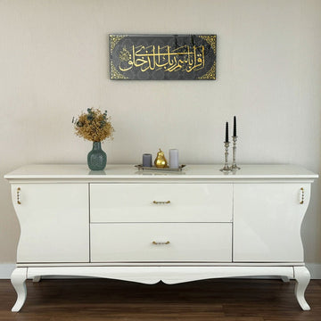 Surah Al-Alaq glass wall art above a white cabinet with a vase and candlesticks