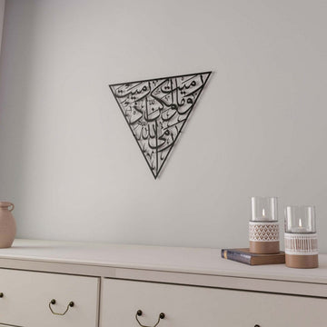 Black Surah Al-Anfal 17 triangle metal wall art above a sideboard with two glass candle holders