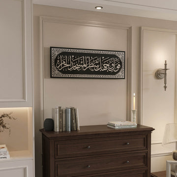 Silver Surah Baqarah 144 mihrab verse glass wall art beside a wall sconce above a dark dresser