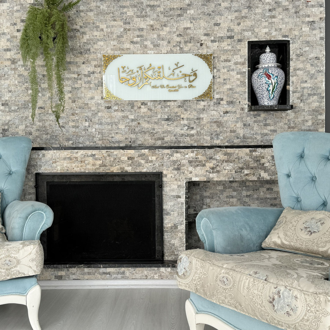 Gold Acrylic on Solid White Surah Naba Verse 8 tempered glass wall art above a fireplace beside a blue armchair