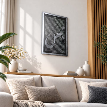 Silver Surah Yaseen wall art seen at an angle beside a wooden slat wall panel