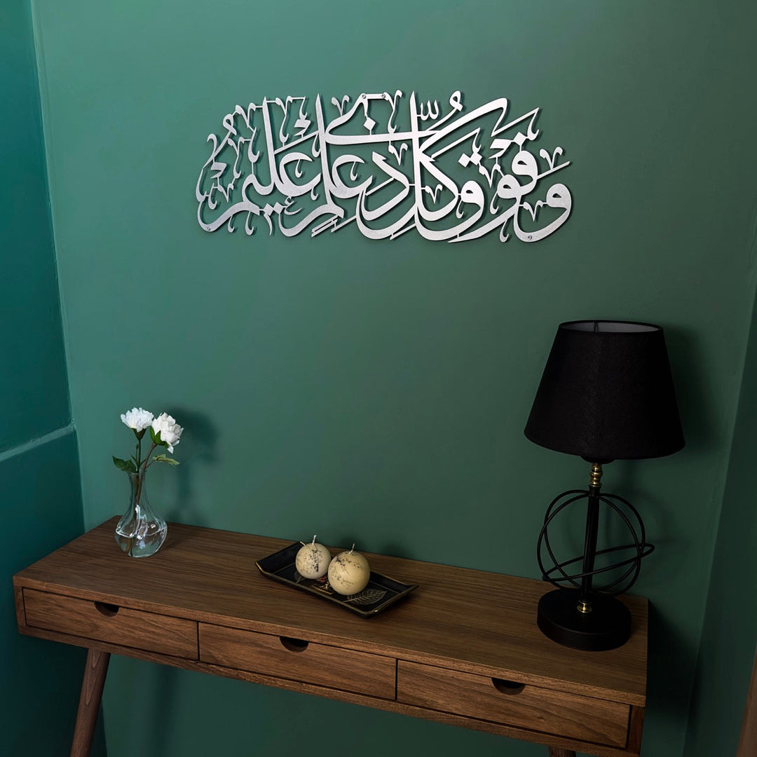 Surah Yusuf Ayat 76 Matte Silver metal calligraphy on a green wall with a table lamp