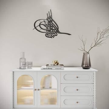 Metall-Wandkunst Tughra Bismillah in Schwarz, an einer hellen Wand über einem weißen Sideboard mit Glastüren