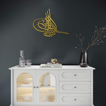 Metall-Wandkunst Tughra Bismillah in Gold, an einer dunklen Wand über einem weißen Sideboard mit Glastüren