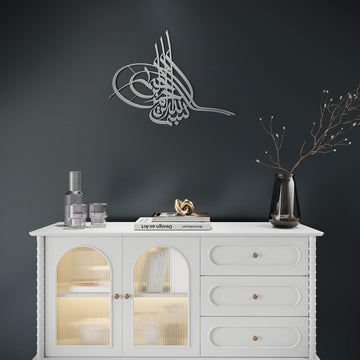 Metall-Wandkunst Tughra Bismillah in Silber, an einer dunklen Wand über einem weißen Sideboard mit Glastüren