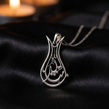 Silver Tulip Mashallah pendant on black satin with candles glowing behind
