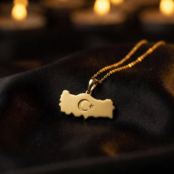 Gold Turkiye map necklace on black satin with candles softly lit behind