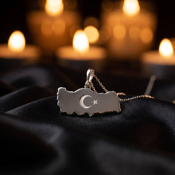 Silver Turkiye map necklace on black satin with candles glowing in the background