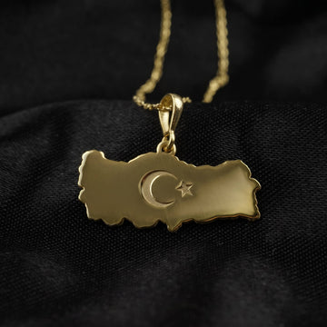 Gold Turkiye map pendant with a crescent and star, on a chain over black fabric