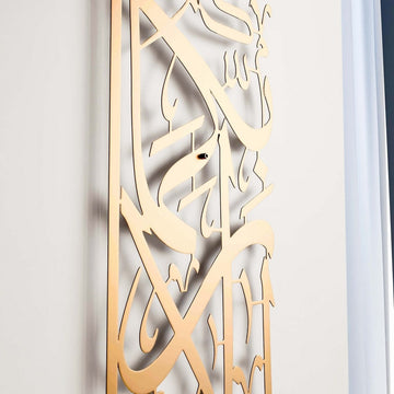 Vertikale Metall-Wandkunst Sure Rahman Vers 13 in Mattgold, schräger Blick auf die Kalligrafie mit sanftem Wandschatten