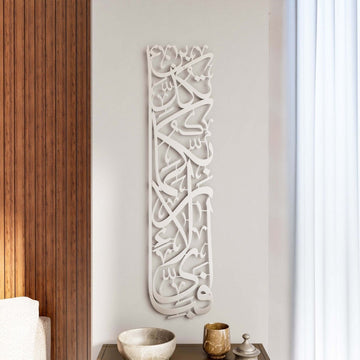 Vertikale Metall-Wandkunst Sure Rahman Vers 13 in Mattsilber an einer hellen Wand neben einem Vorhang
