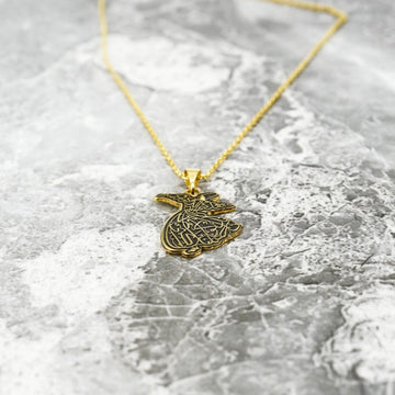 Goldener Derwisch-Anhänger mit Kette auf einer grauen Marmoroberfläche liegend