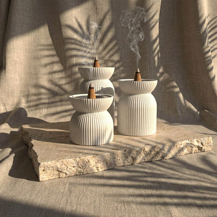 Two white incense burners with wooden sticks on a stone surface, with a neutral background.