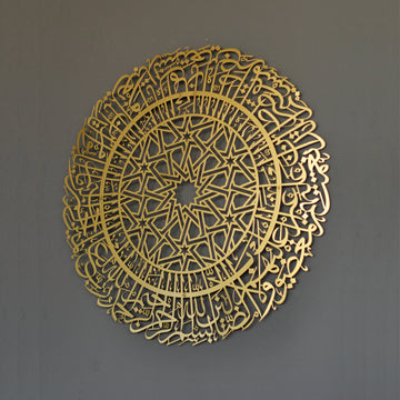 Goldene runde Metall-Wandkunst mit Sure Al-Fatihah an einer grauen Wand, leicht schräg