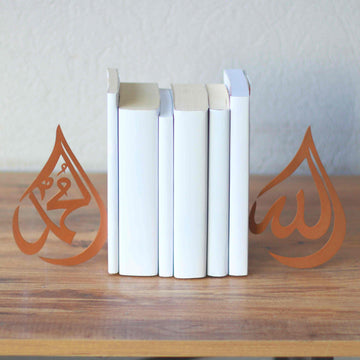Kupferfarbene Buchstützen im Tropfendesign Allah und Mohammed (Friede sei mit ihm) neben weißen Büchern auf einem Holztisch